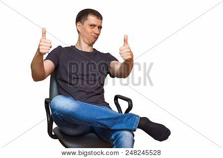 Positive Young Caucasian Man With A Funny Face, Dressed In Casual Clothes Without Shoes, Sitting On 