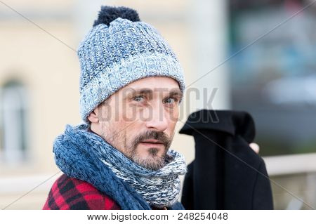 Portrait Of White Man In Winter Knitted Hat And Scarf. White Guy On Street Hold Black Coat. Bearded 
