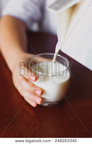 Fresh, Homemade, Store Milk Is Poured Into A Mug. The Boy Is Holding A Mug. The Jet Of Milk. Closeup