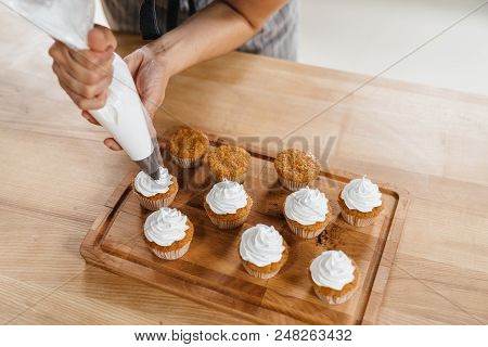 Confectioner Woman Decorates A Capcake Or Muffin With Whipped Cream Through A Pastry Bag.