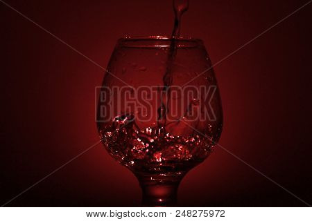 Simple Still-life Photo Of Whisky Glass, Water Jet And Dim Red Light