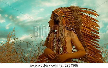 Child playing at sunset dressed as an American Indian, wearing an Indian feather plume and breastplate. Field of wheat and nature