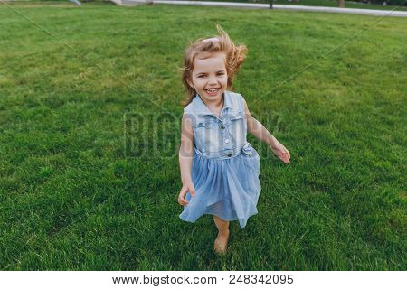 Laughing Little Cute Child Baby Girl In Denim Dress Walking And Running, Have Fun On Green Grass Law