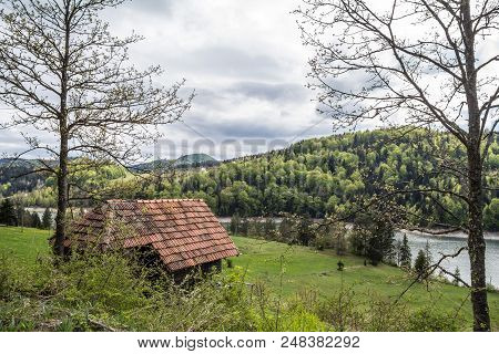 Zaovine Valley And Lake Seen From The Top Of A Cliff, With A Mountain Village House In The Foregroun