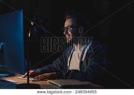 Smiling Young Programmer In Eyeglasses Working With Desktop Computer At Night