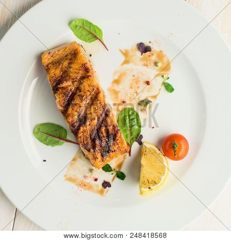 Tasty Cooked Steak On A White Plate With Bay Leaves And Herbs On A White Wooden Table. Brown Backgro