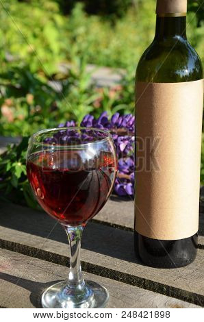 Red Wine Poured Into Wine Glass On Background Of Green Tree Leaf Foliage. Purpie Flower