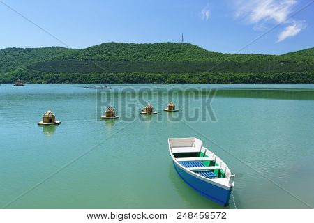 Bright Blue Empty Rowing Boat And Duck Houses On The Emerald Water Of The Mountain Lake Abrau-durso