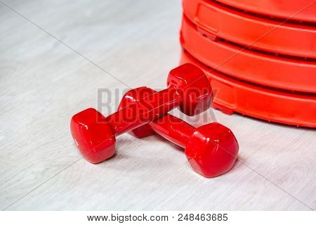 Red Modern Dumbbells And Pancakes For Dumbbells In The Foreground On A Wooden White Floor