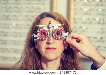 In Optician Shop- Optican Checking Eyes Of Woman For New Glasses