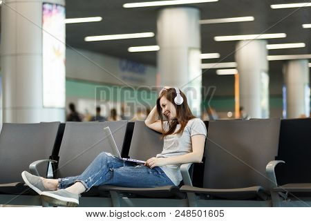 Young Smiling Traveler Tourist Woman With Headphones Listening Music Working On Laptop, Wait In Lobb