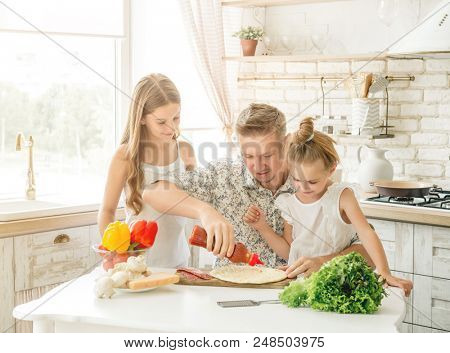 dad with two little daughters preparing pizza in the kitchen