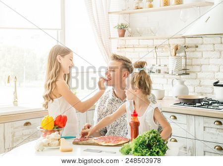 Dad with two small daughters preparing pizza with mushrooms in the kitchen