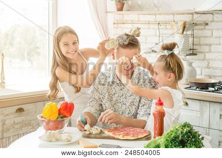 Dad with two small daughters preparing pizza with mushrooms in the kitchen
