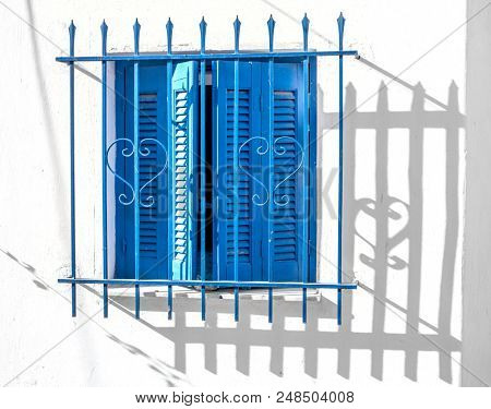Closed blue wooden window shutters with wrought security grate on white wall in Greece