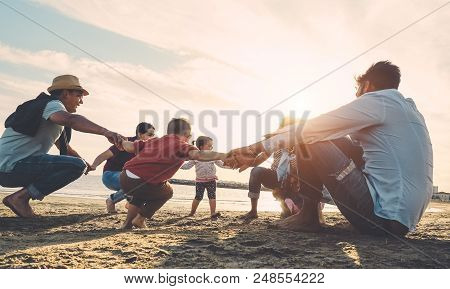Family Friends Having Fun On The Beach At Sunset - Fathers, Mothers, Children And Uncles Playing Tog