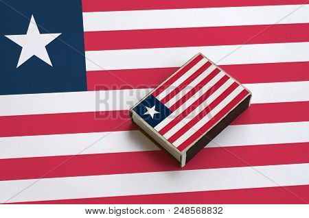 Liberia Flag  Is Pictured On A Matchbox That Lies On A Large Flag.