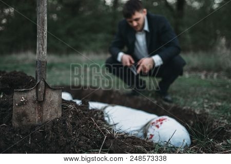 Slayer against grave, victim wrapped in a canvas