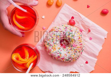 Child's Hand Takes Sweet Pastryfrosted Sprinkled Donut On Pink Background. Tubules For A Cocktail. S