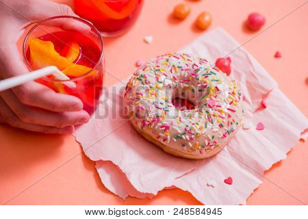 Child's Hand Takes Sweet Pastryfrosted Sprinkled Donut On Pink Background. Tubules For A Cocktail. S