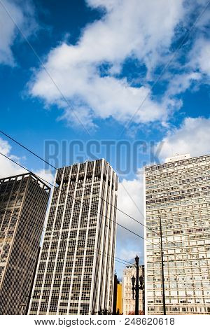 An Electric Wire Passes By This Vertical Image Of Business Buildings In A Blue Sky With Clouds Day