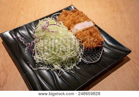 Fried Pork Tongkatsu With Vegetable In Black Ceramic Plate On Wood Table.