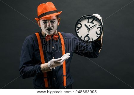 Scary Clown Pantomime With A Clock In His Hands, On A Dark Background.