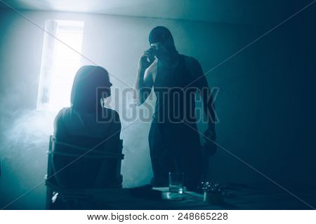 Kidnapper And His Victim Are In Dark Room With Small Window. He Is Standin In Front Of It And Talkin