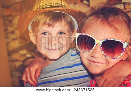 Toned Picture Of A Girl In Sunglasses, Hugs Her Younger Brother.