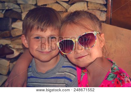 Toned Picture Of A Girl In Sunglasses, Hugs Her Younger Brother.