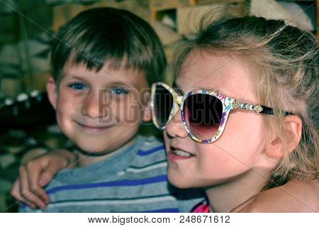 Toned Picture Of A Girl In Sunglasses, Hugs Her Younger Brother.