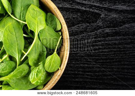 Fresh Baby Spinach Leaves In A Wooden Bowl Top View On Black Wood Background