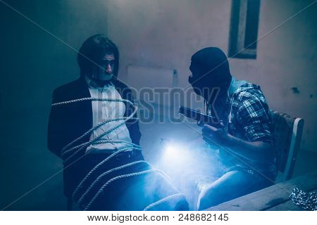 Serious Man In Black Mask Is Holding Pistol In On Hand And Lights In Another One. He Is Looking At H