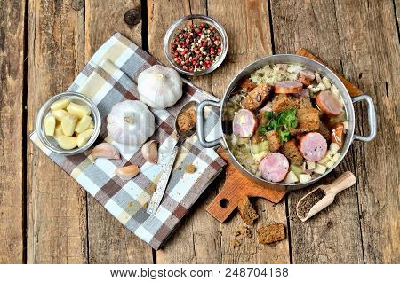 View From Above Of Garlic Soup In An Old Saucepan, Sausage, Fresh Garlic Bulbs, Cloves, Colored Pepp