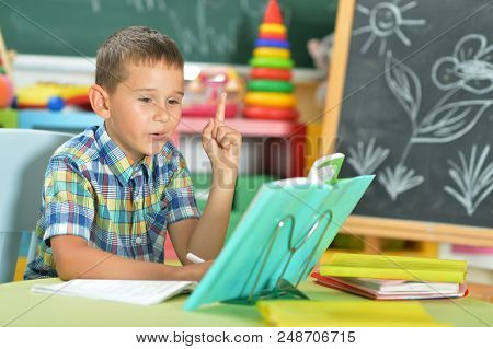Young Boy Doing Homework And Pointing Up With Finger In Classroom