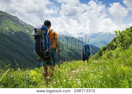 Tourists With Hiking Backpacks In Mountain Hike In Svaneti On Summer Day. Young Guys Go Along The Fo