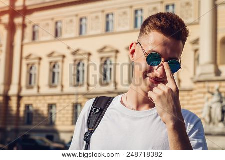 Handsome College Man Checking His Glasses Against The University. Happy Guy Student With Backpack Sm