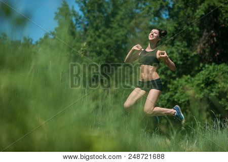 Young Woman Jumping On Background Of Trees. The Girl Is Engaged In Sports.