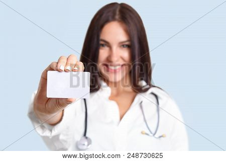 Small White Blank Card With Copy Space In Hand`s Of Pretty Nurse. Lovely Brunette Professional Cheer