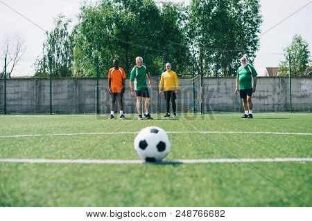 Selective Focus Of Football Ball And Multicultural Elderly Men On Green Football Field
