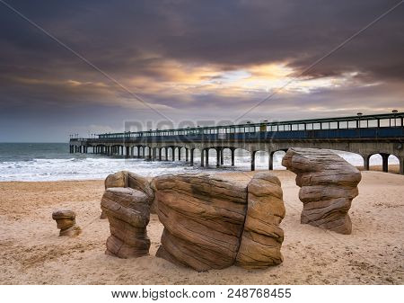 Sun Shines Through Clouds At Sunset Over Boscombe Pier And Beach