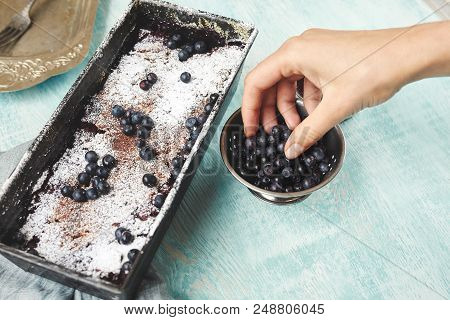 Berry Crumble In The Baking-tin And Small Bowl With Blueberries On The Blue Wooden Table. Woman Spri
