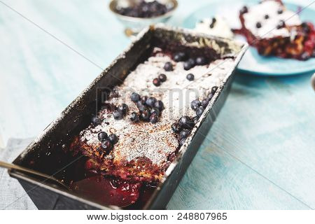 Closeup Berry Crumble In The Baking-tin And Small Bowl With Blueberries On The Blue Wooden Table. To