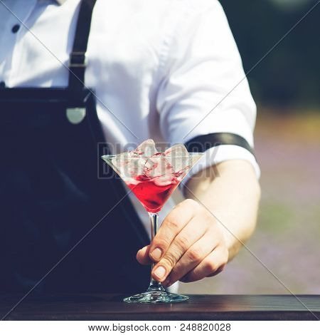 Close-up Bartender Holding A Martini Glass With Red Cold Cocktail Outdoors, Selective Focus, Toned I