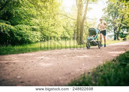 Running Woman With Baby Stroller Enjoying Summer Day In Park. Jogging Or Power Walking Supermom, Act