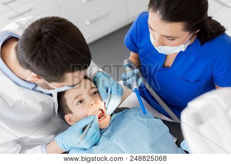 medicine, dentistry and healthcare concept - dentist with mouth mirror and probe checking for kid patient teeth at dental clinic