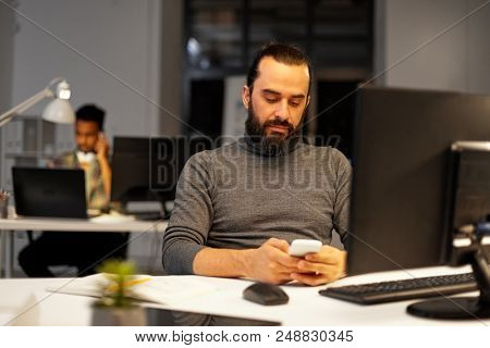 deadline, technology and people concept - creative man with smartphone and computer working at night office