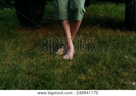 Bare Feet To Stand On The Green Grass. In Green Shorts Near The Car