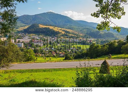 A Modern City At The Foot Of A Mountain Covered With Dense Forest, Green Grass, Blue Sky. Masto For 