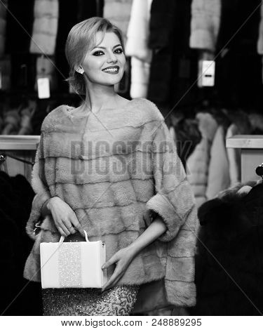 Girl With Happy Face Wears Furry Coat On Clothes Rack Background. Elegance And Glamour Concept. Lady